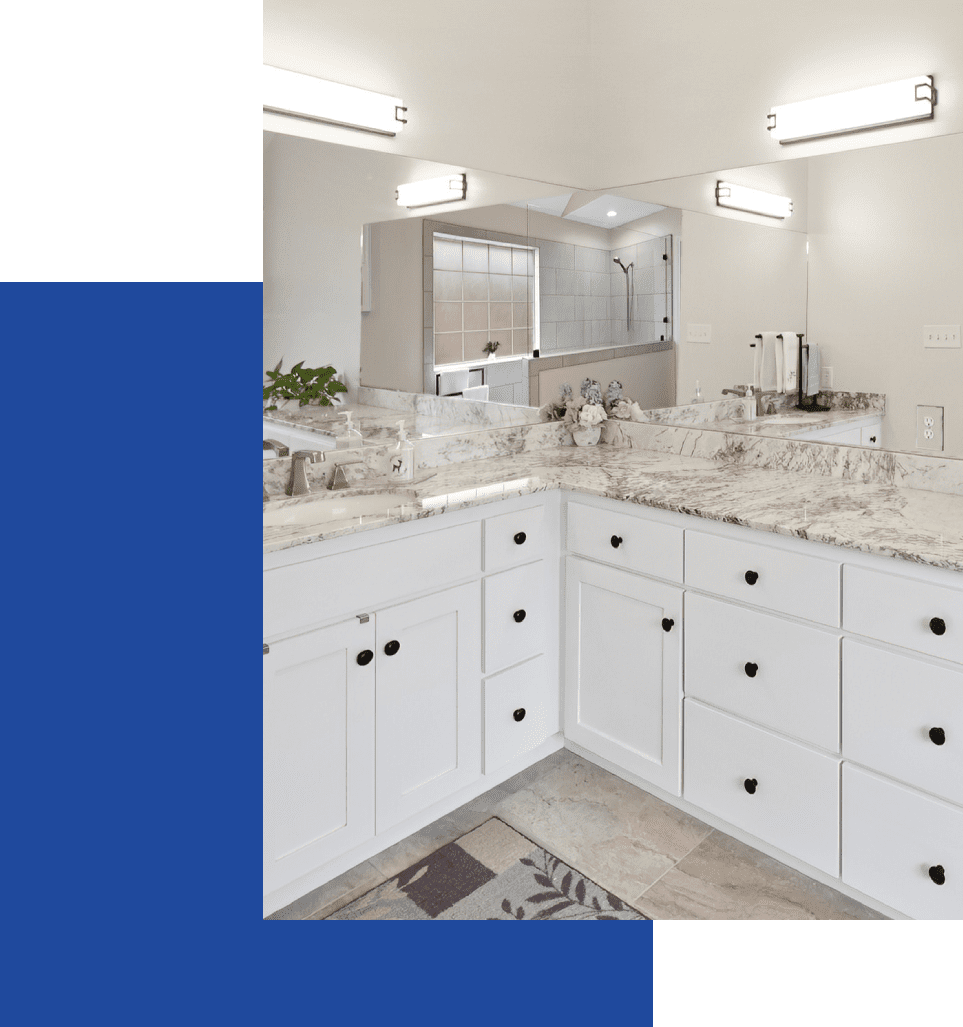 A bathroom with white cabinets and marble counter tops.